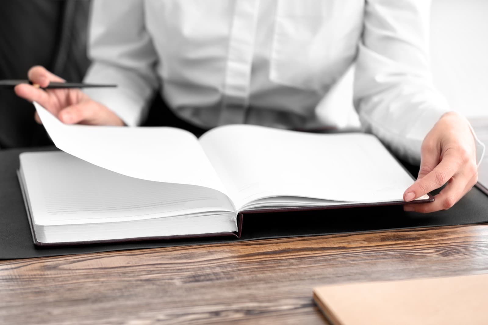 Ofis masasında açık bir kayıt defterinin sayfalarını çeviren kişi