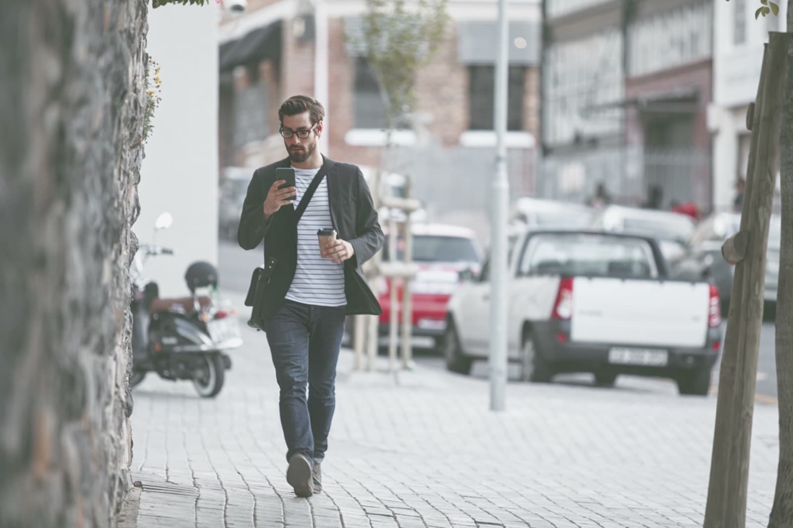 Şehir sokağında yürürken telefonuna bakan ceket giymiş bir adam